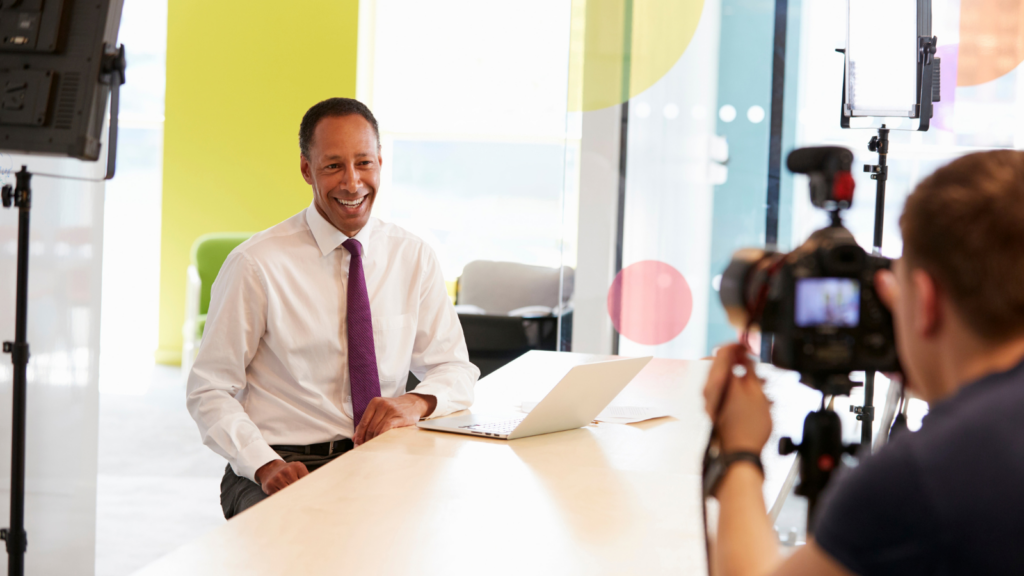 Executive smiling at a laptop while a camera operator films an interview