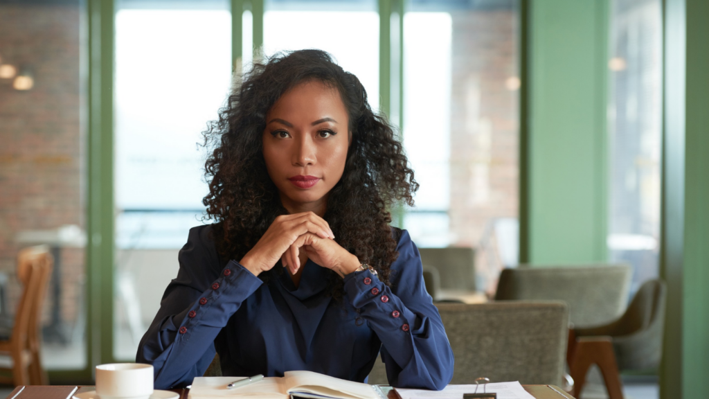 Businesswoman with curly hair at her desk, hands clasped, looking at the camera