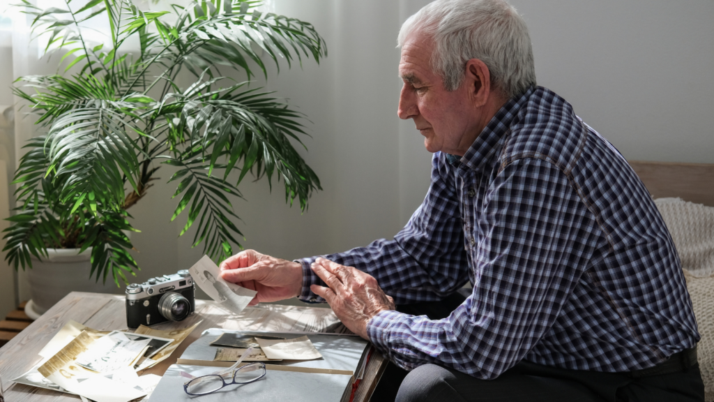 Older man looking through old photographs and a vintage camera at a table
