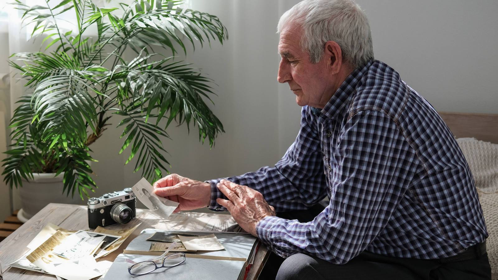 Older man looking through old photographs and a vintage camera at a table