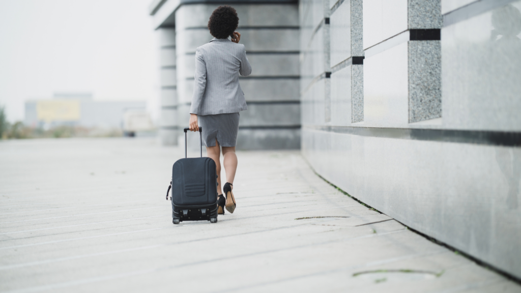 Businesswoman walking outside with rolling luggage, seen from behind